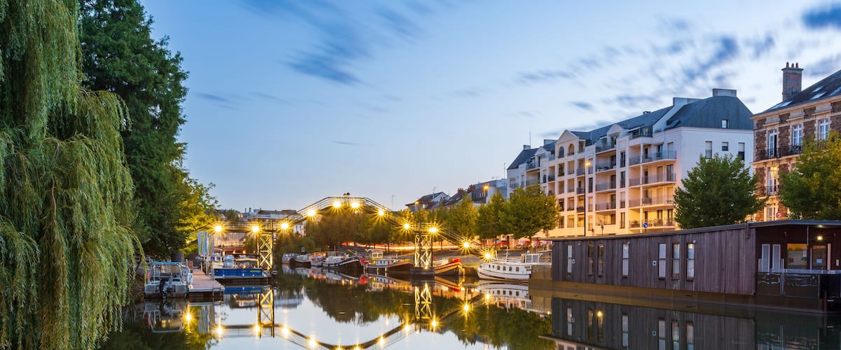 Une rivière paisible où se reflètent les bâtiments et les arbres, avec des bateaux amarrés le long de la rive.