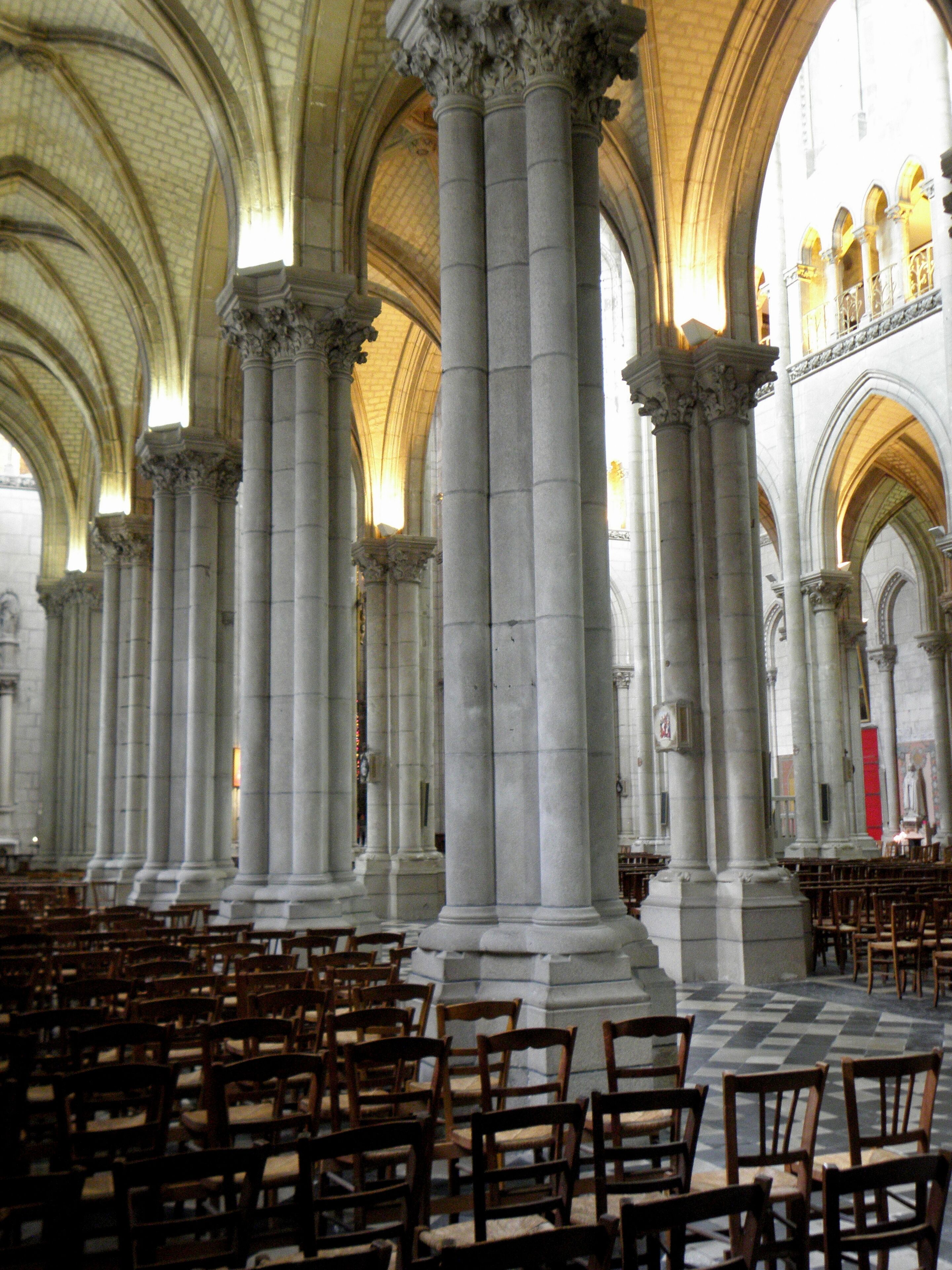 A grand cathedral interior with high vaulted ceilings, large stone columns, and rows of wooden pews.