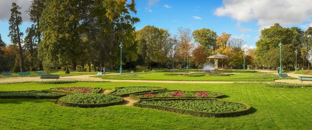 A well-manicured park with geometric flower beds, a gazebo, and a fountain.