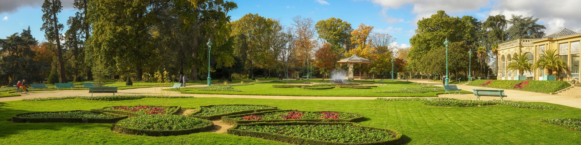 Un parc aux jardins bien entretenus, avec des parterres de fleurs aux formes géométriques, un kiosque et une fontaine.