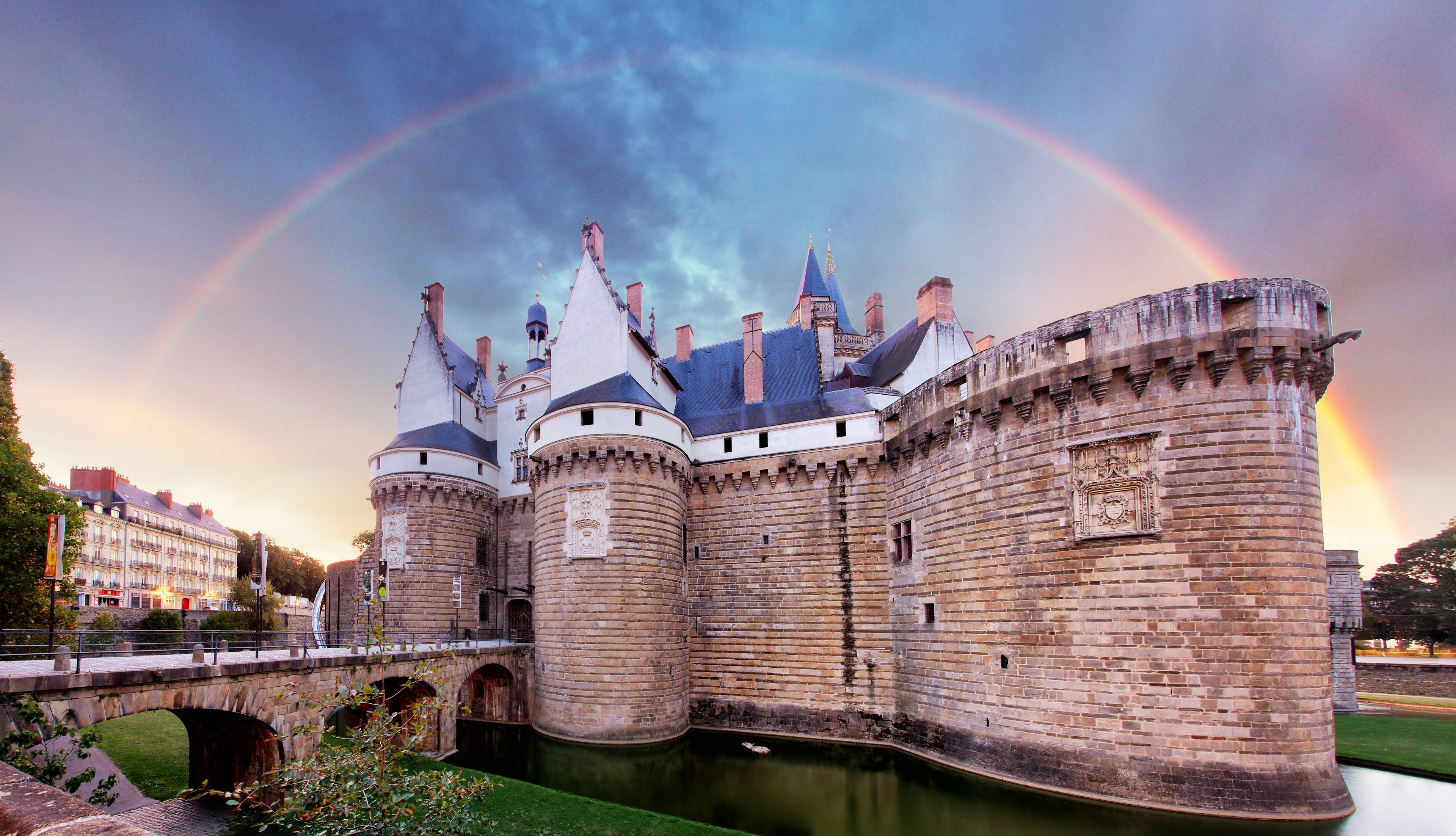 Un château historique, doté d’un fossé, d’un pont et d’un arc-en-ciel dans le ciel.