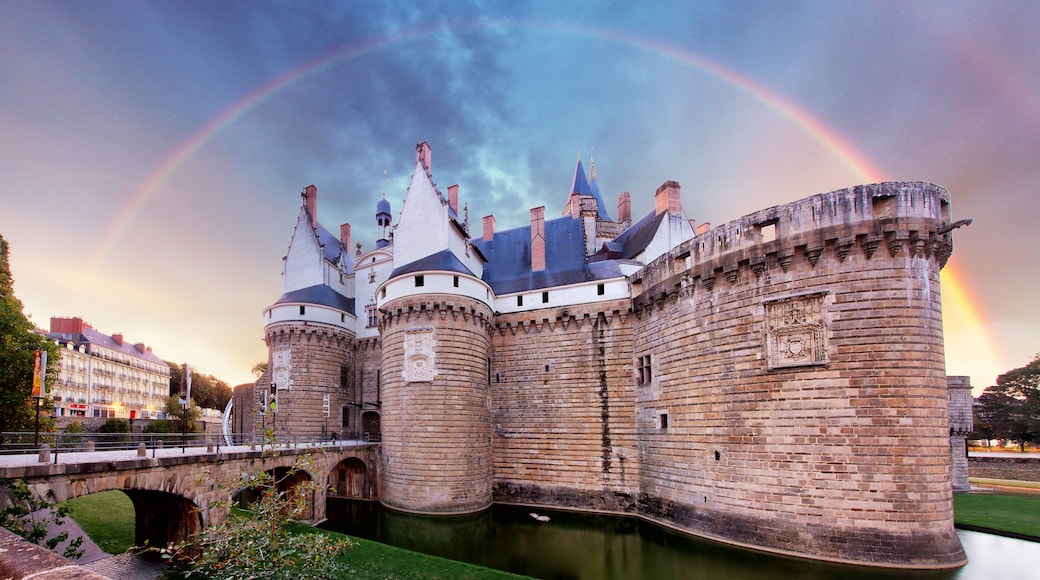 A historic castle with a moat, a bridge, and a rainbow in the sky.