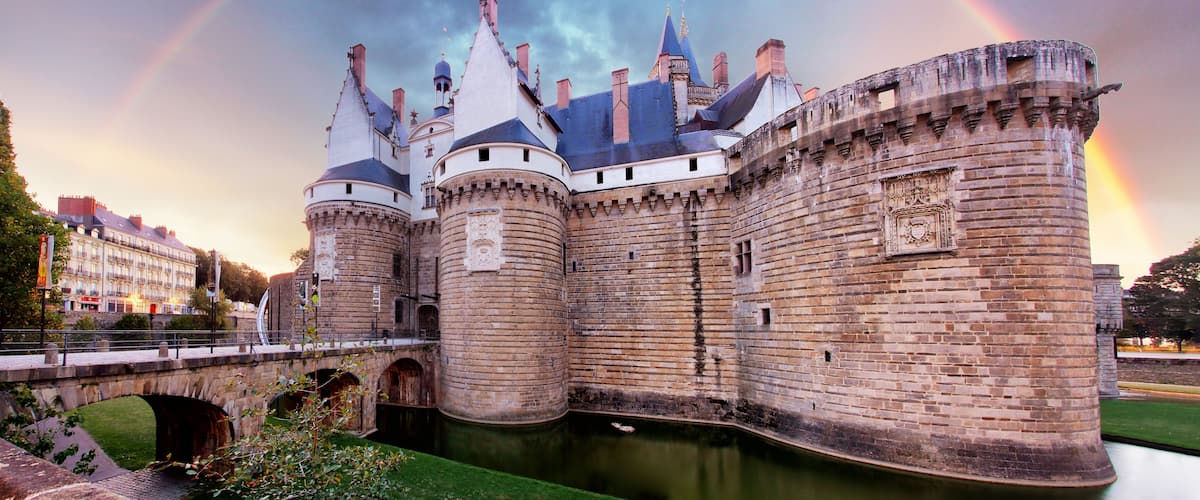 Un château historique, doté d’un fossé, d’un pont et d’un arc-en-ciel dans le ciel.