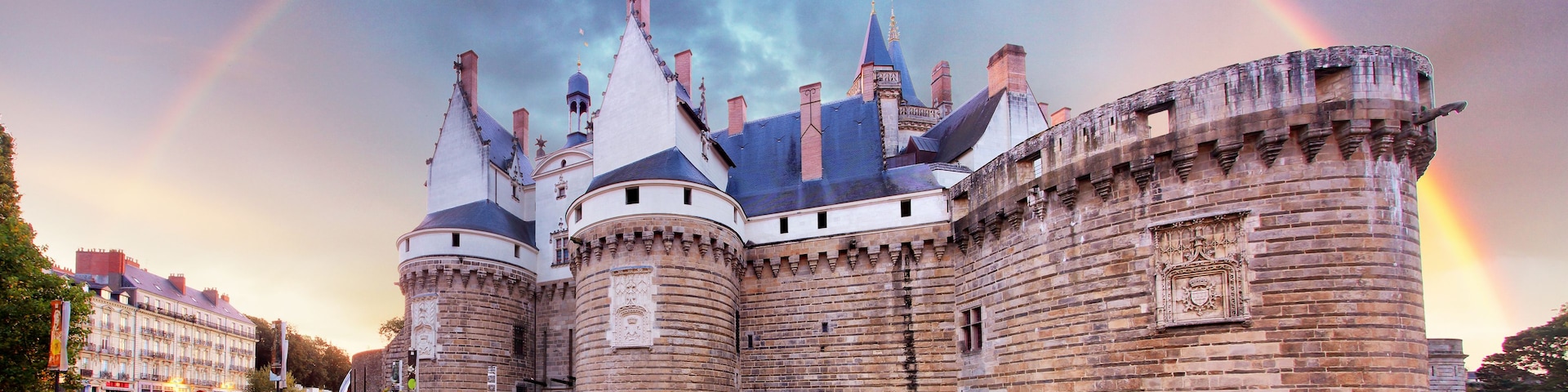 Un château historique, doté d’un fossé, d’un pont et d’un arc-en-ciel dans le ciel.