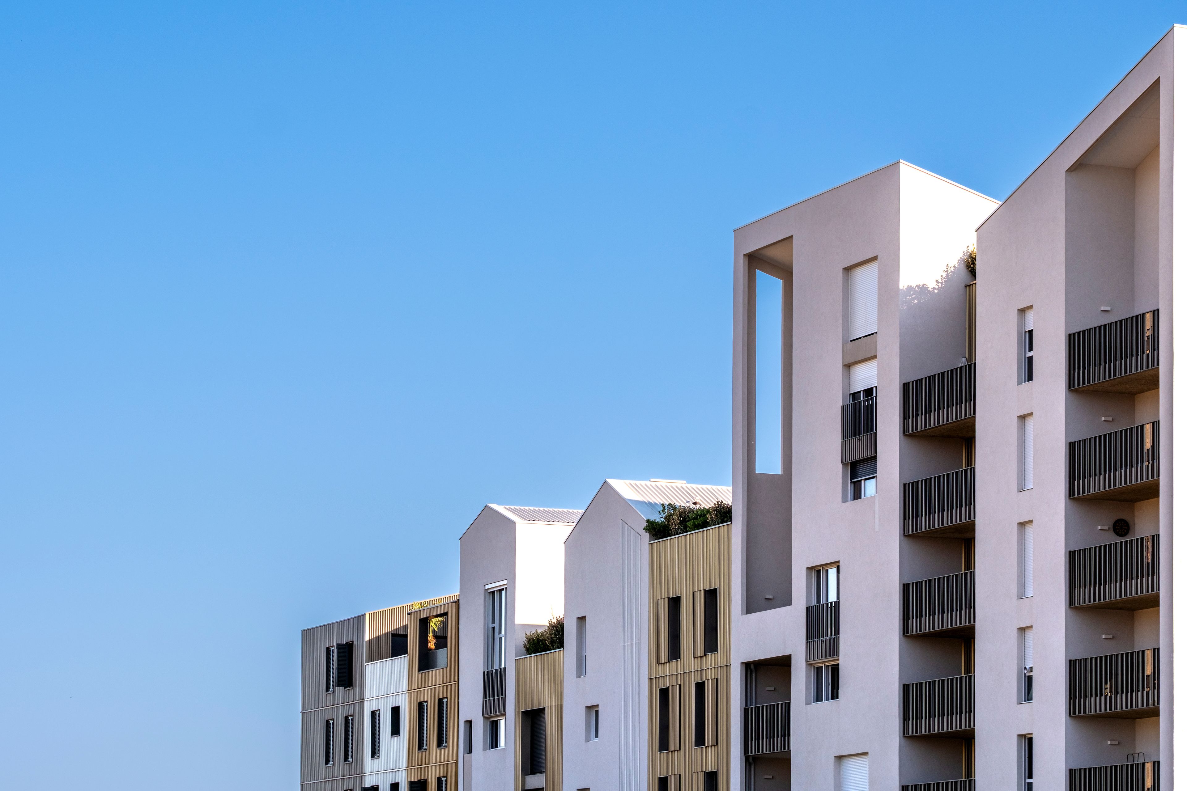 A modern multi-story residential building with balconies and a clear blue sky.