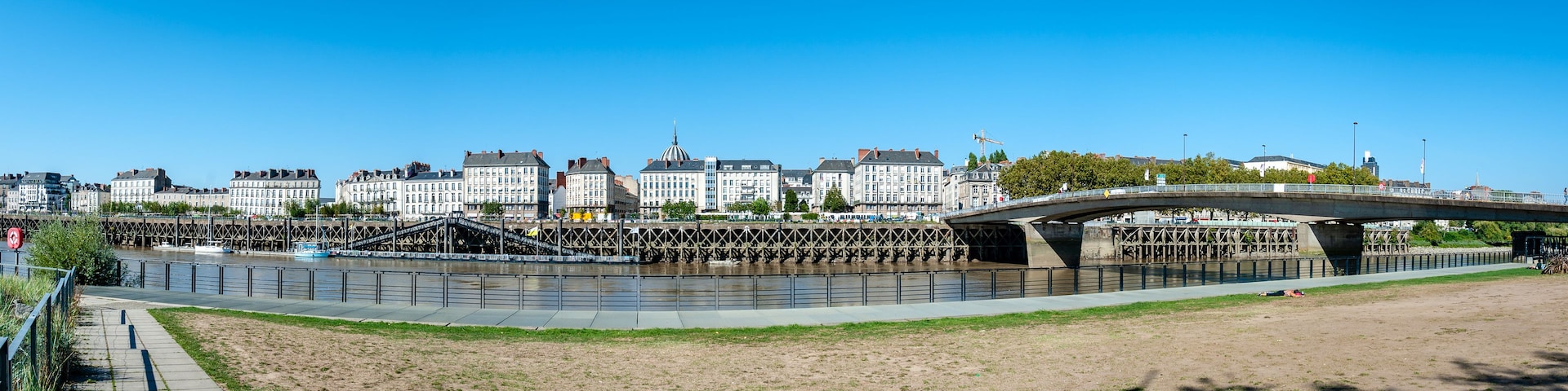 Une rivière traversée par un pont, un paysage urbain avec des bâtiments historiques et un ciel bleu dégagé.