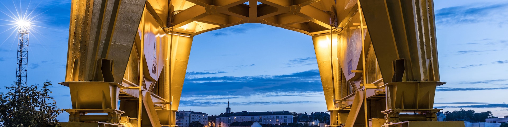 Un grand pont métallique illuminé, visible au crépuscule, avec une vue sur la ville en arrière-plan.