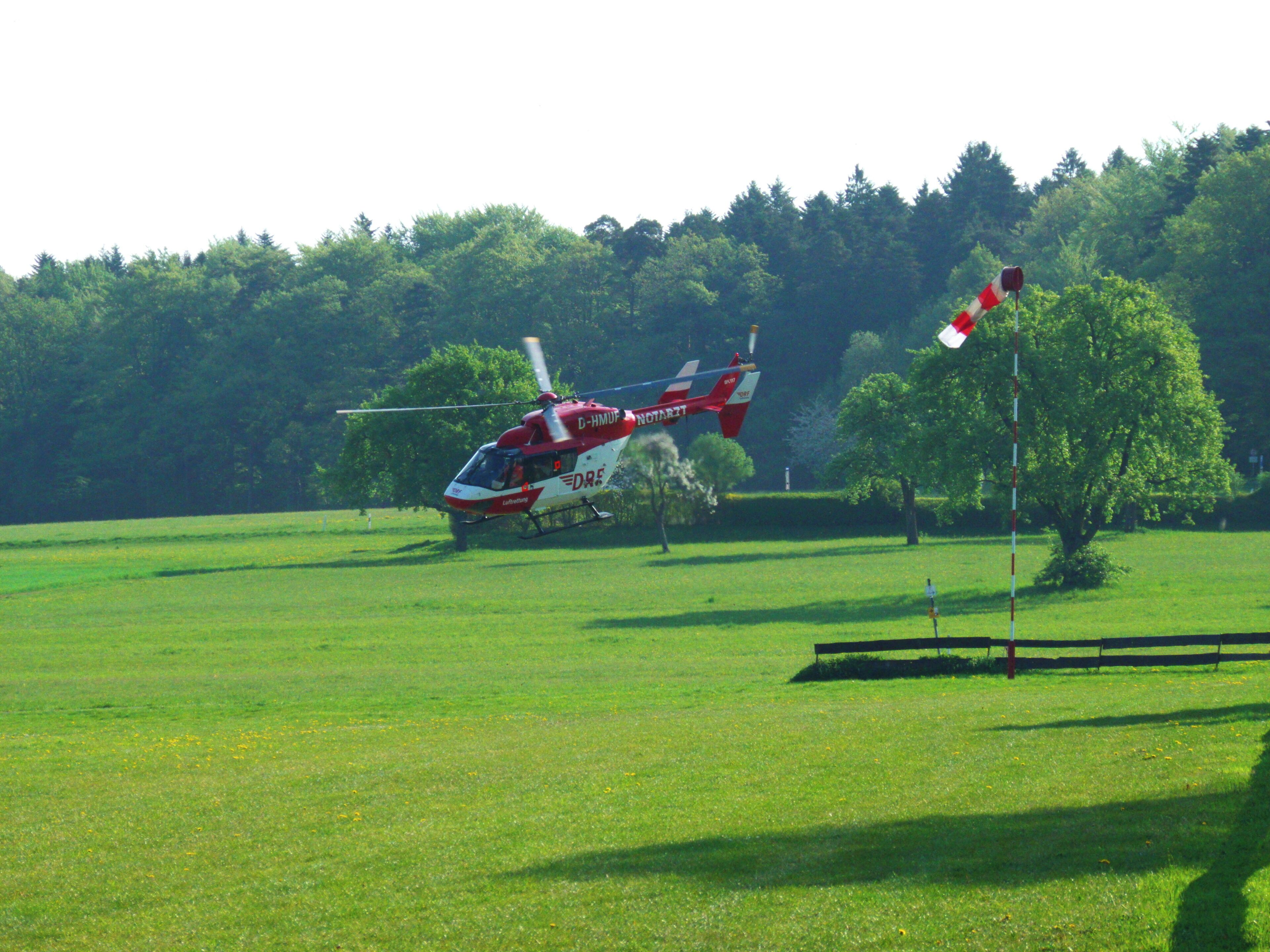 A red and white helicopter in a grassy field with trees in the background.