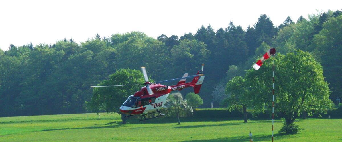 A red and white helicopter in a grassy field with trees in the background.