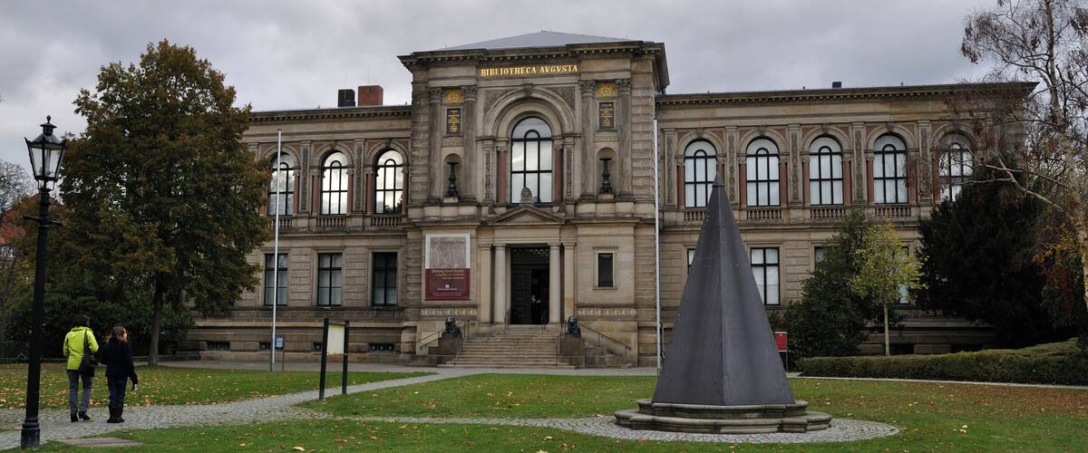 A historic building with a prominent entrance, a statue in front, and a well-maintained lawn.