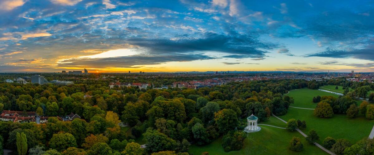 Ein weiter Panoramablick über eine Stadt mit einem Park, einem großen Gewässer und einem Sonnenuntergang.