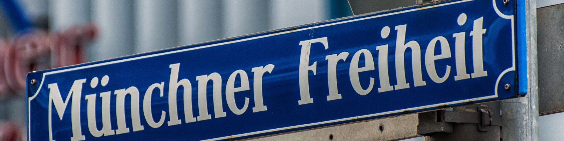 Placa de rua com o texto 'Münchner Freiheit' fixado em um poste de metal.