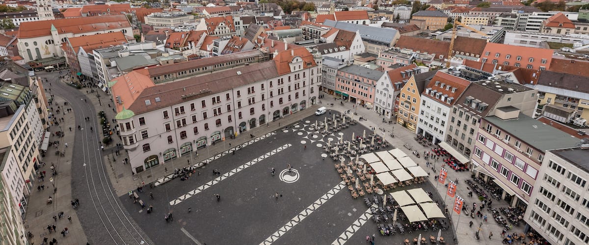 Una plaza animada con edificios históricos, una fuente central y zonas de estar al aire libre.