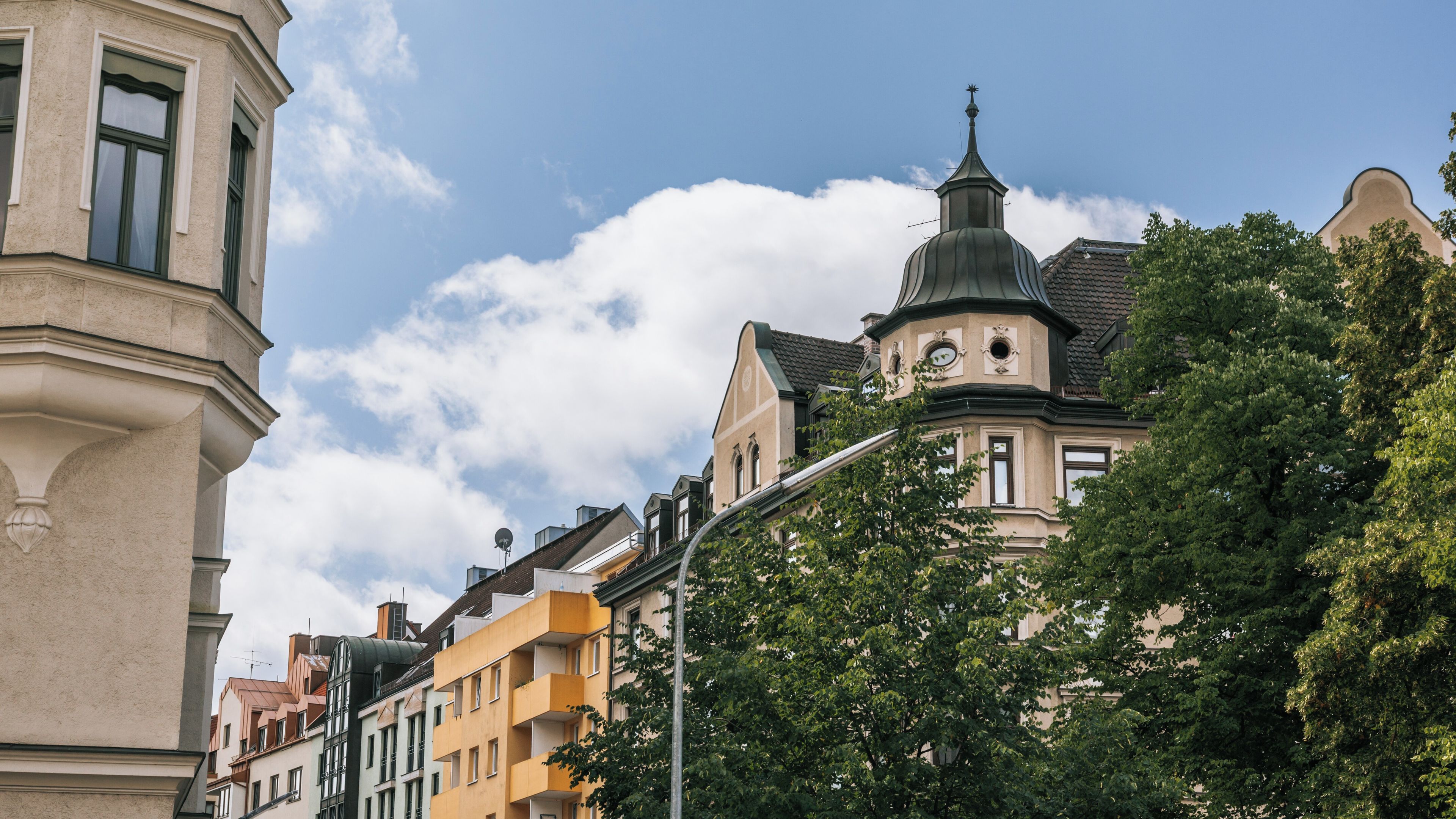 Um edifício histórico com cúpula verde e torre do relógio, rodeado por árvores e outros edifícios coloridos.