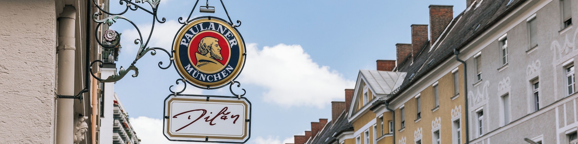 Straßenansicht mit einem Schild für 'Paulaner München' und einem kleineren Schild für 'Jillich'.