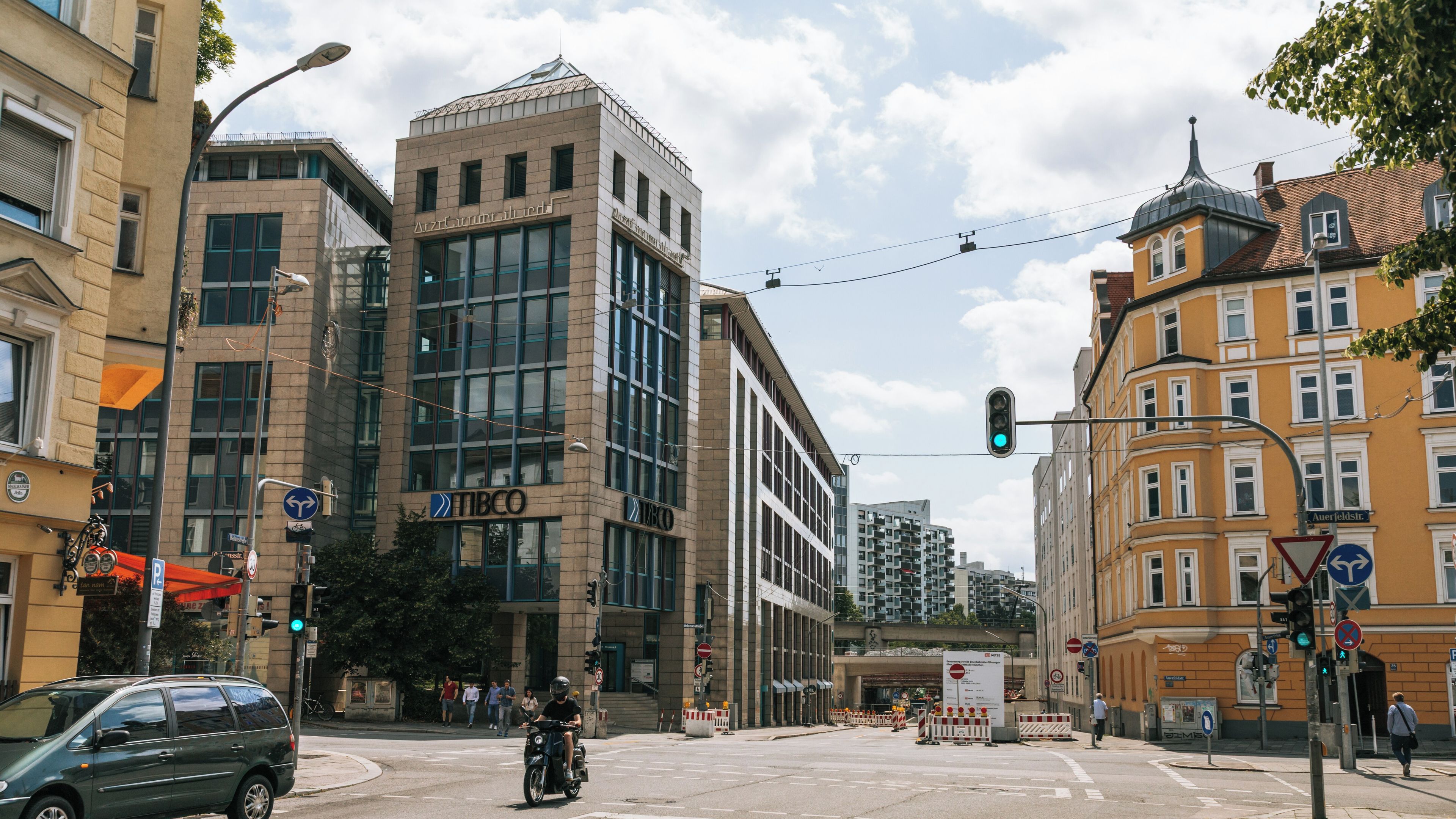 Cruzamento urbano com edifícios modernos, semáforo e uma motocicleta.