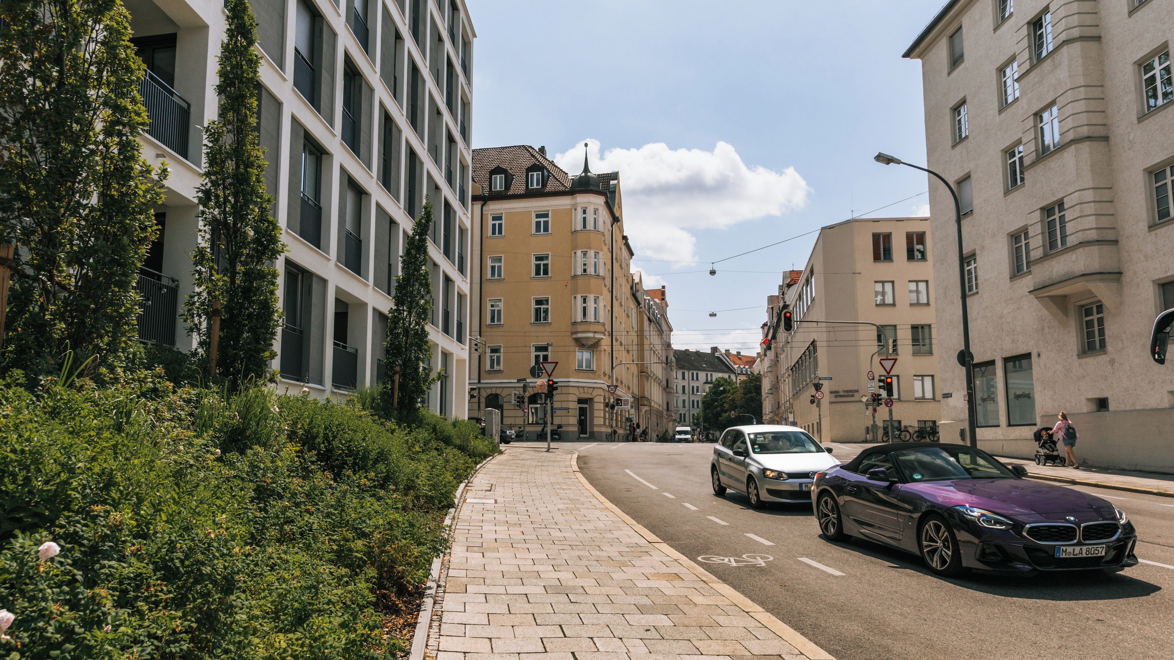 Rua urbana com edifícios modernos, calçada e carros.