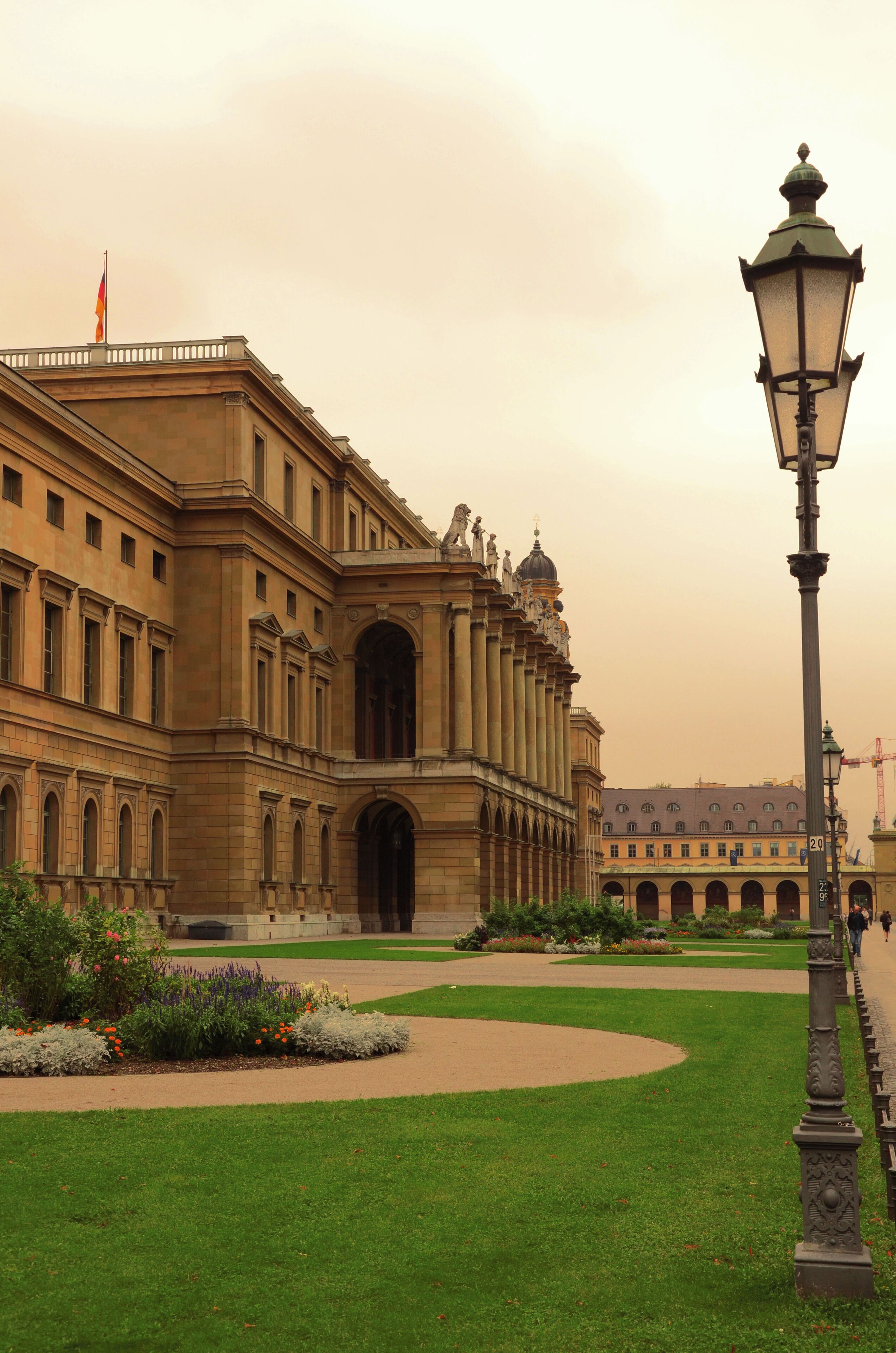 Un edificio imponente con arquitectura clásica, un jardín bien cuidado y un farol de calle.