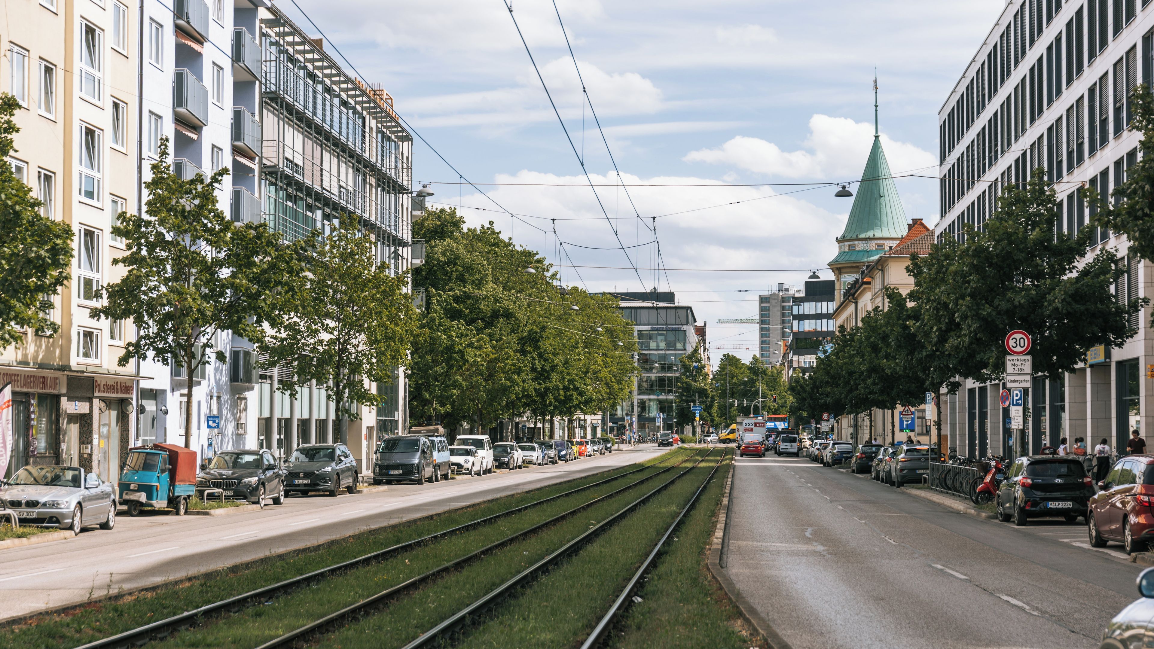 A city street with tram tracks, buildings, and parked cars.