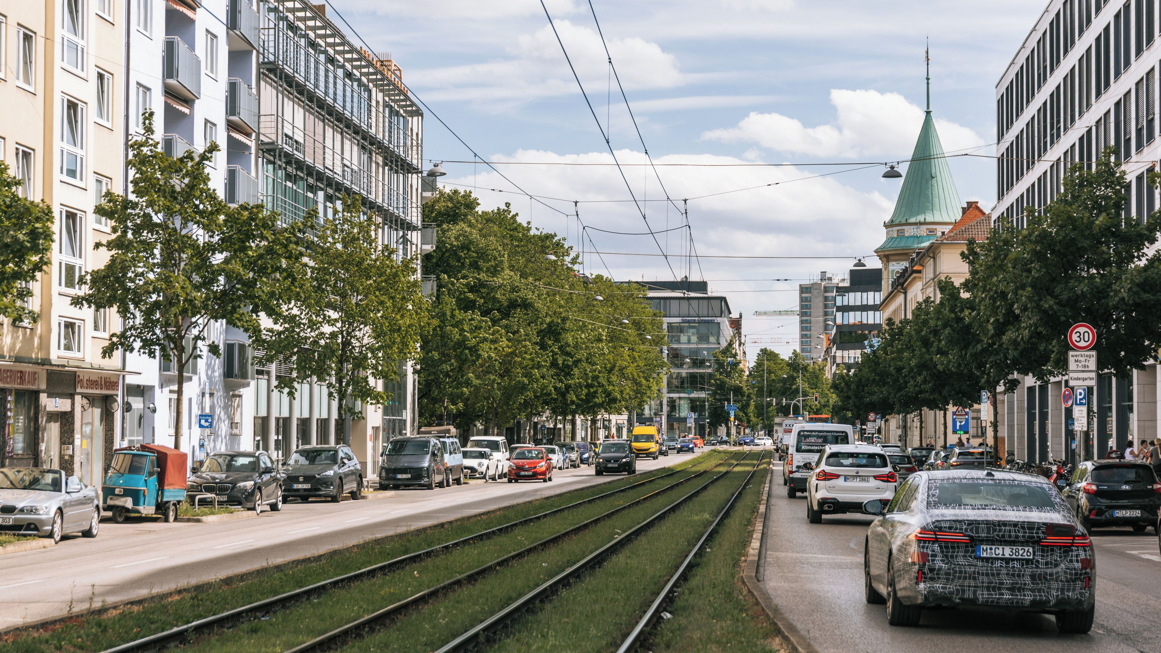 A busy urban street with tram tracks, cars, and buildings.