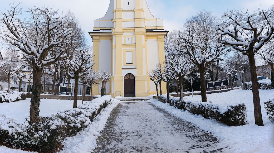 A snow-covered church with a clock tower, surrounded by snow-laden trees and a cobblestone path.