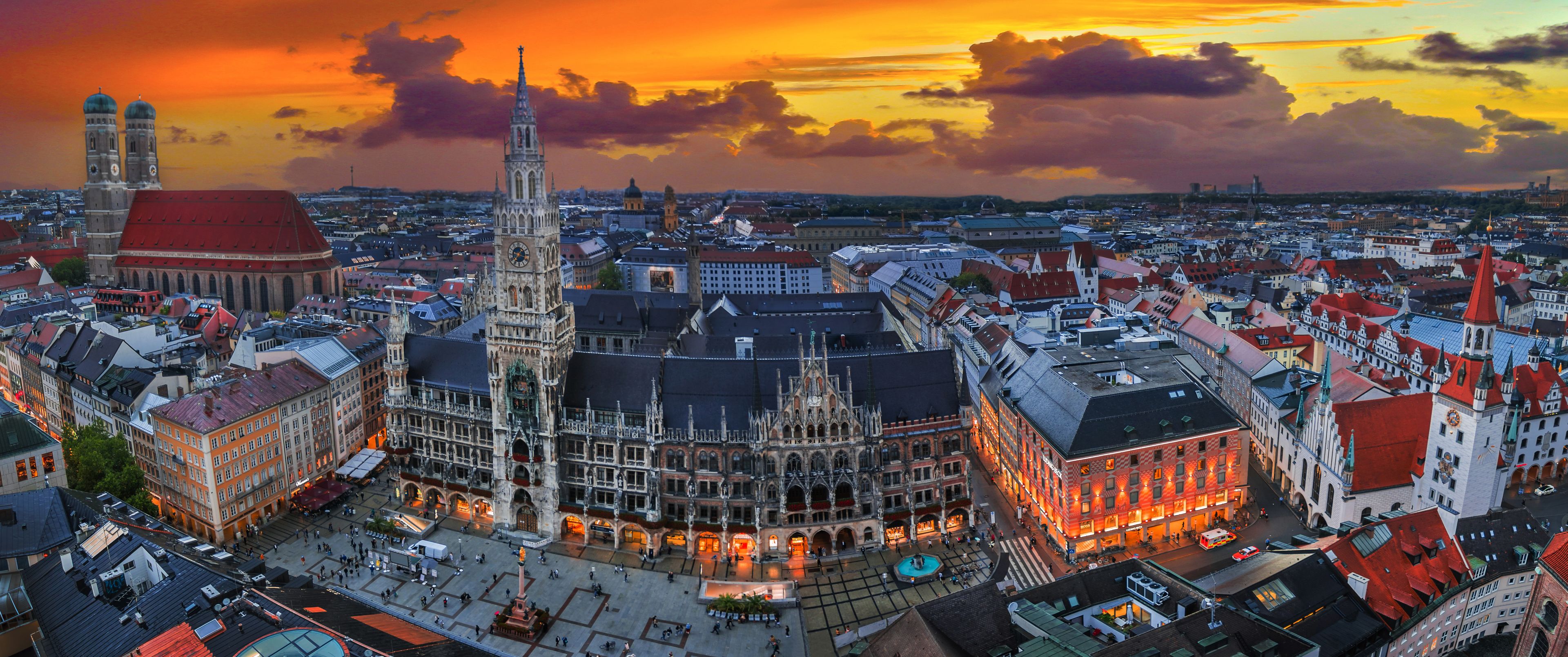 Paisagem urbana com uma catedral imponente e uma torre alta, cercada por edifícios históricos e um céu ao pôr do sol.