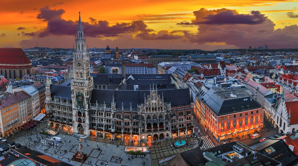 Paisagem urbana com uma catedral imponente e uma torre alta, cercada por edifícios históricos e um céu ao pôr do sol.