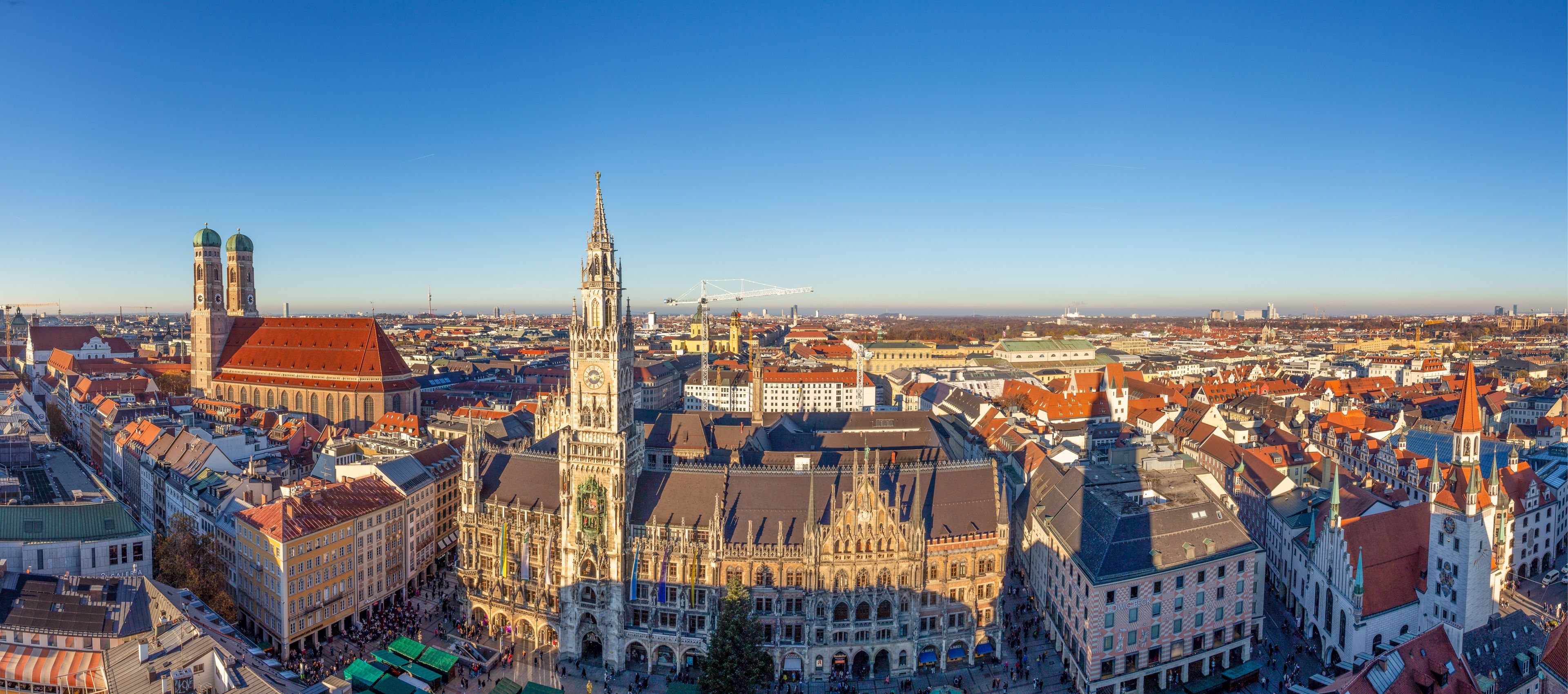 Vista panorâmica de uma cidade histórica com arquitetura gótica marcante, incluindo uma alta torre do relógio e uma catedral com detalhes intrincados.
