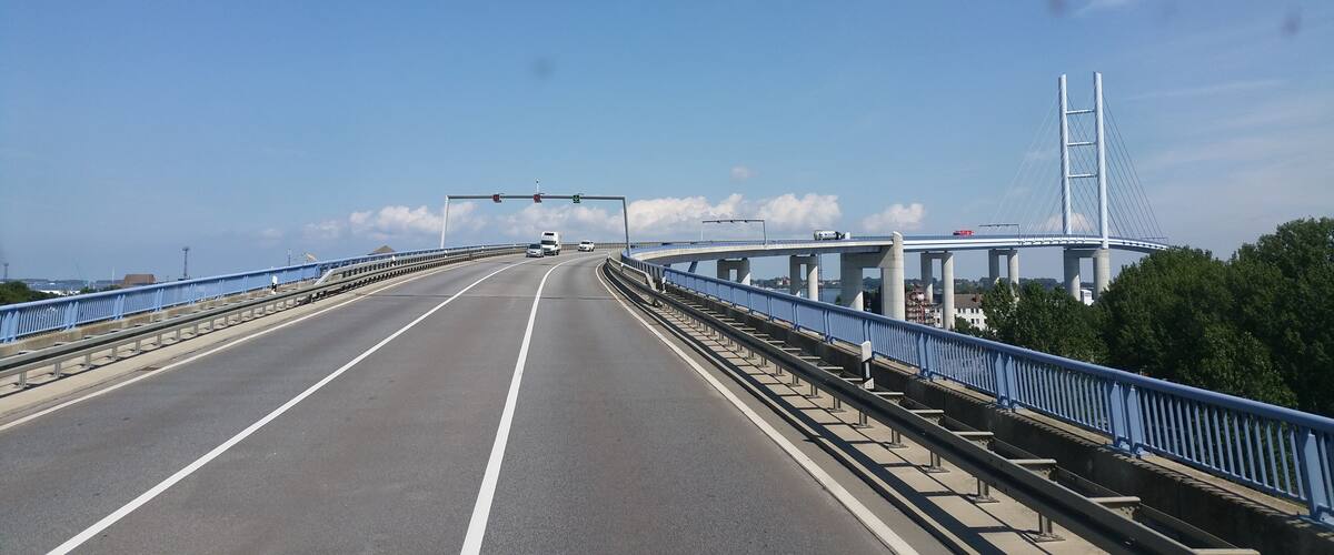 A multi-lane highway with a blue metal railing, a large cable-stayed bridge, and a clear blue sky.