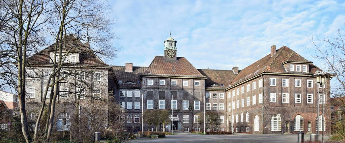 A large, historic building with a prominent clock tower, surrounded by trees and a well-maintained lawn.