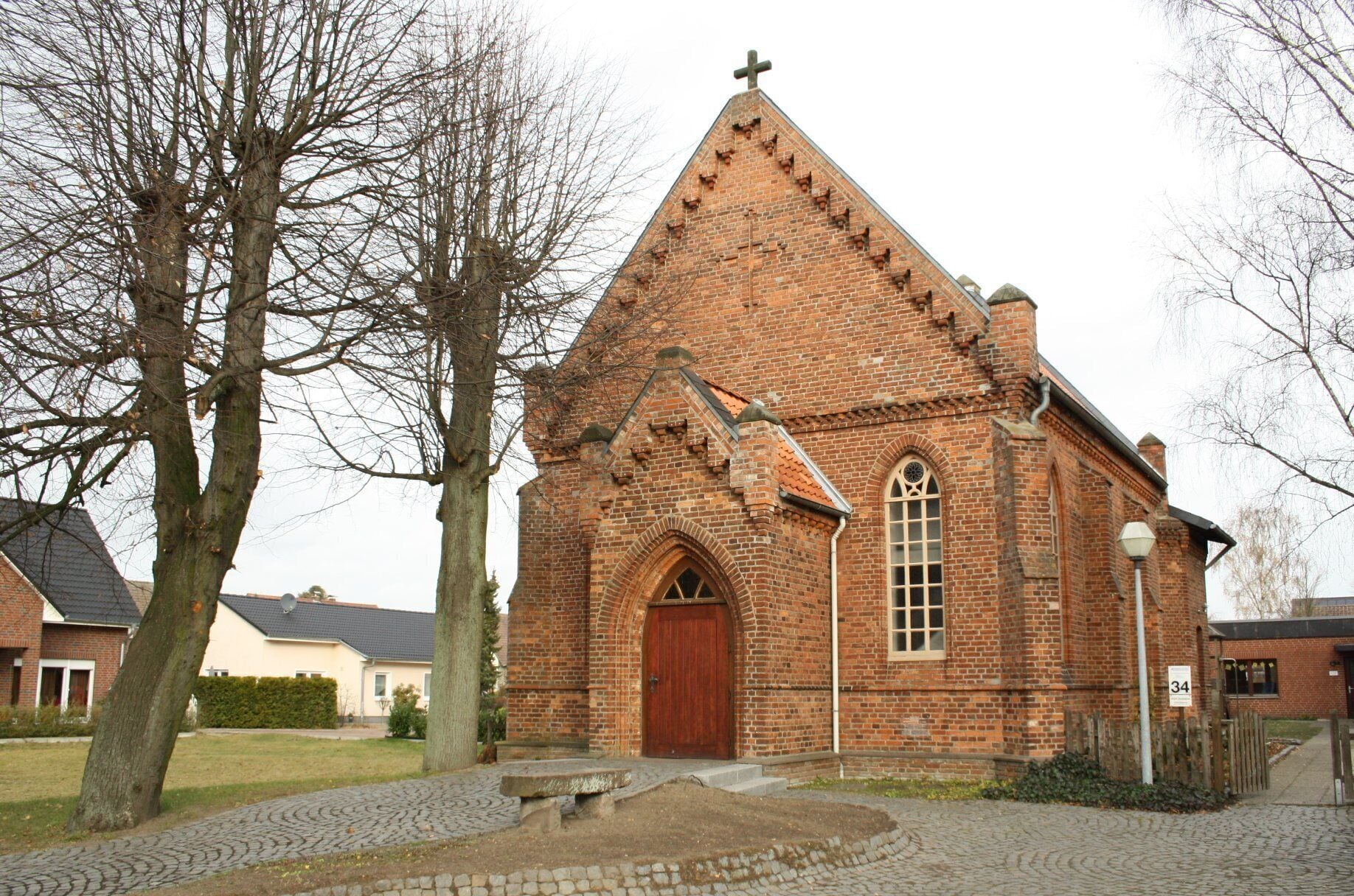 A brick church with a cross on top, a large arched window, and a wooden door.