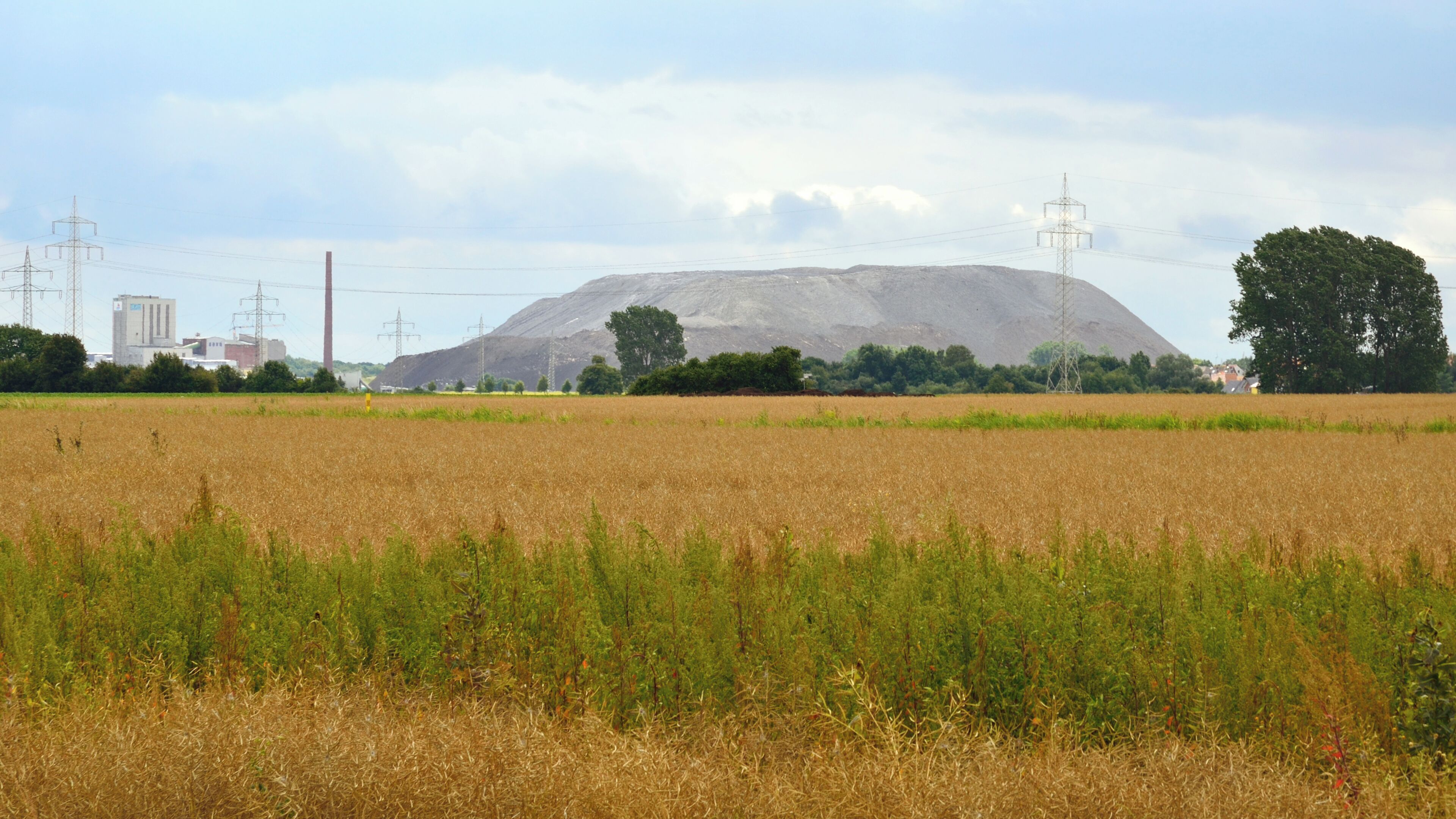 A large hill in a field with power lines and a building in the background.