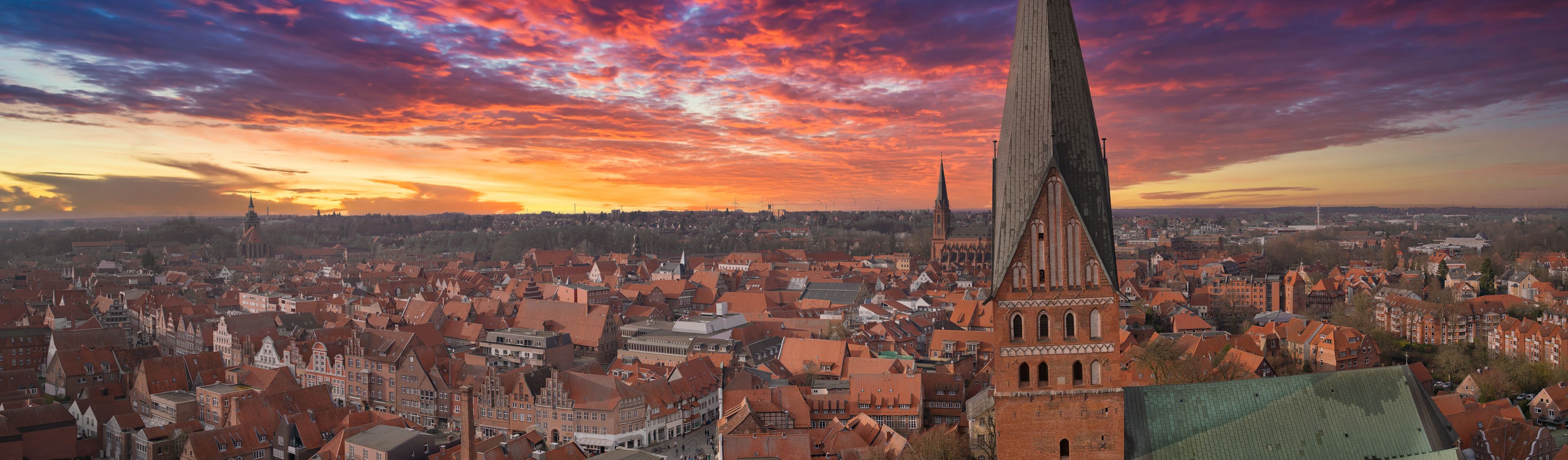 A cityscape with a prominent church tower, dense urban buildings, and a colorful sunset sky.