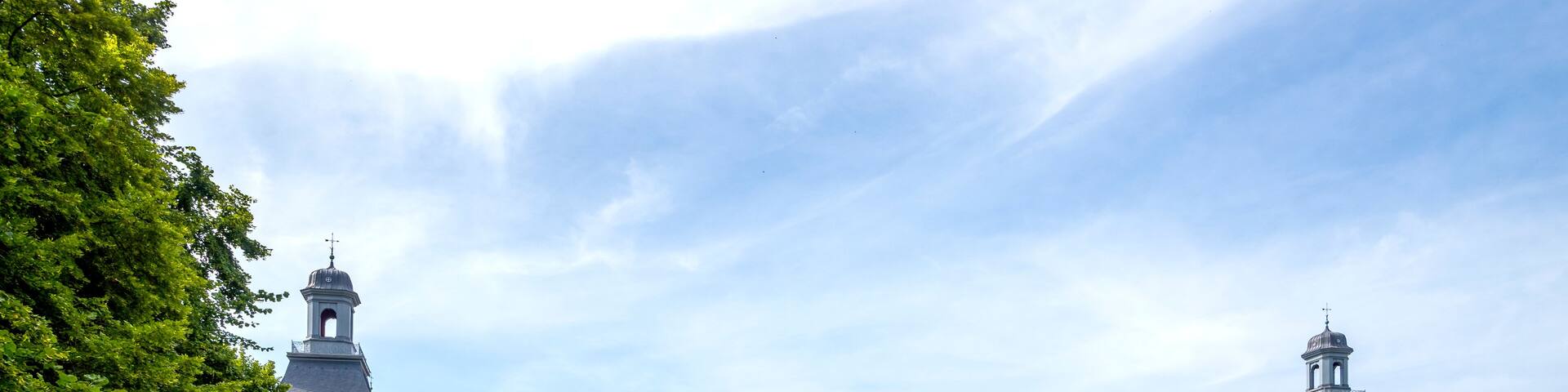 A large yellow building with a clock tower, surrounded by a grassy courtyard with people sitting and walking.