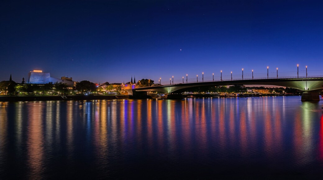 A nighttime river scene with a lit bridge, a boat, and city lights reflecting on the water.