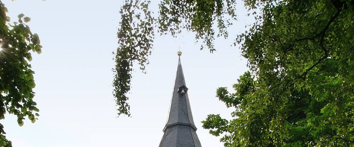 A church with a clock tower, surrounded by greenery and a gravestone.