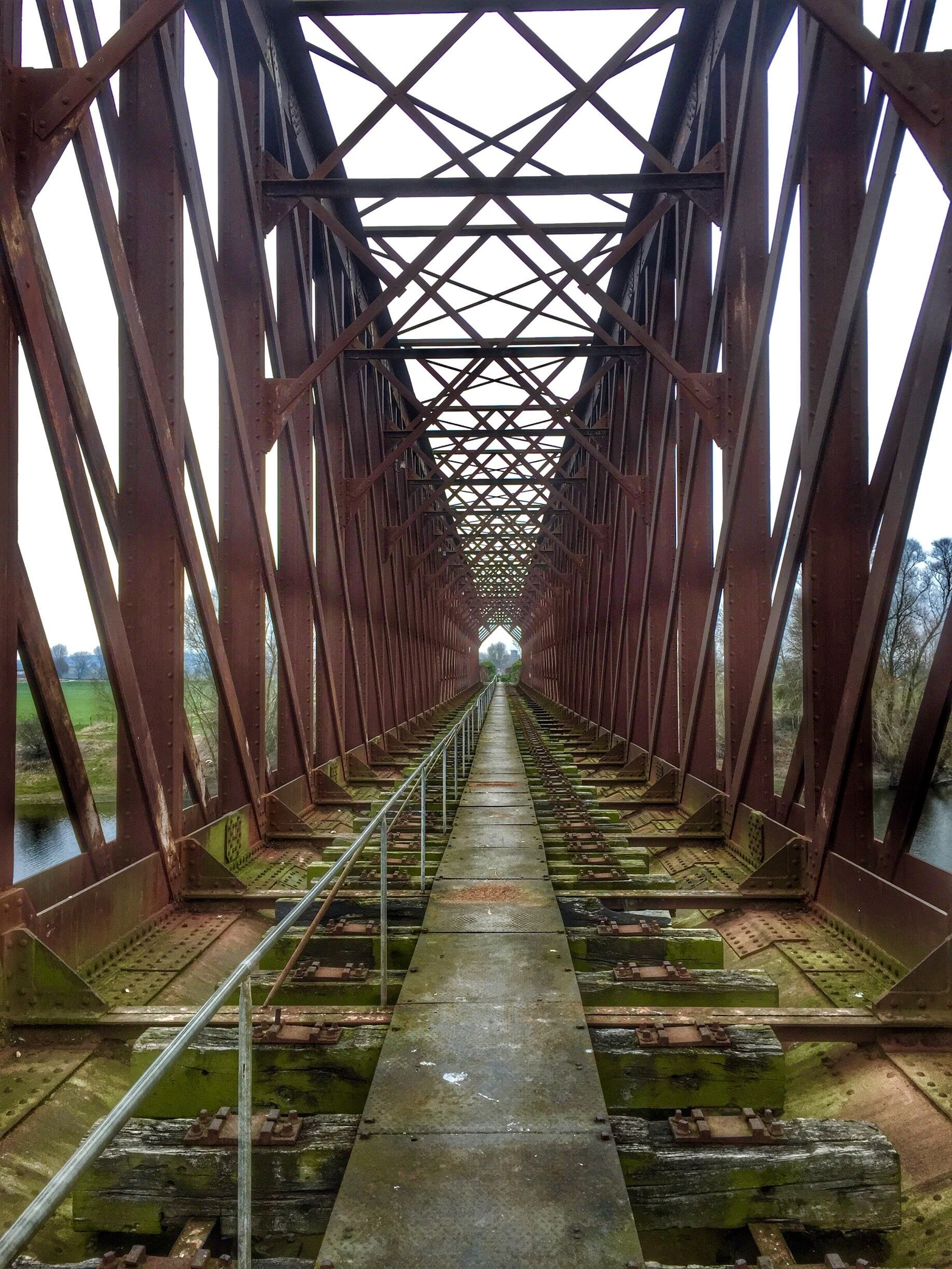 A railway bridge with a metal lattice structure and tracks leading into the distance.