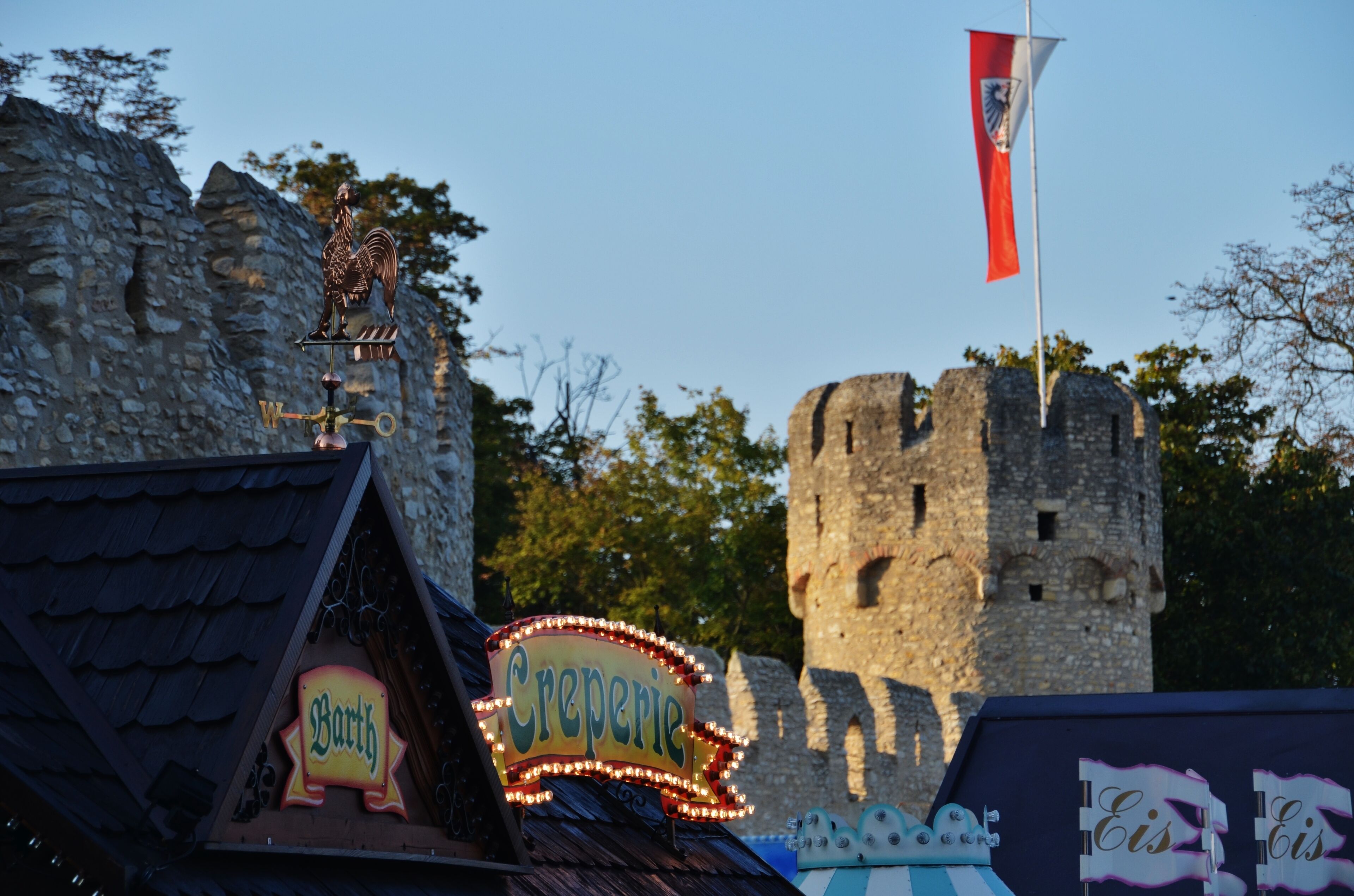 A castle with a flag, a creperie sign, and a rooster statue.