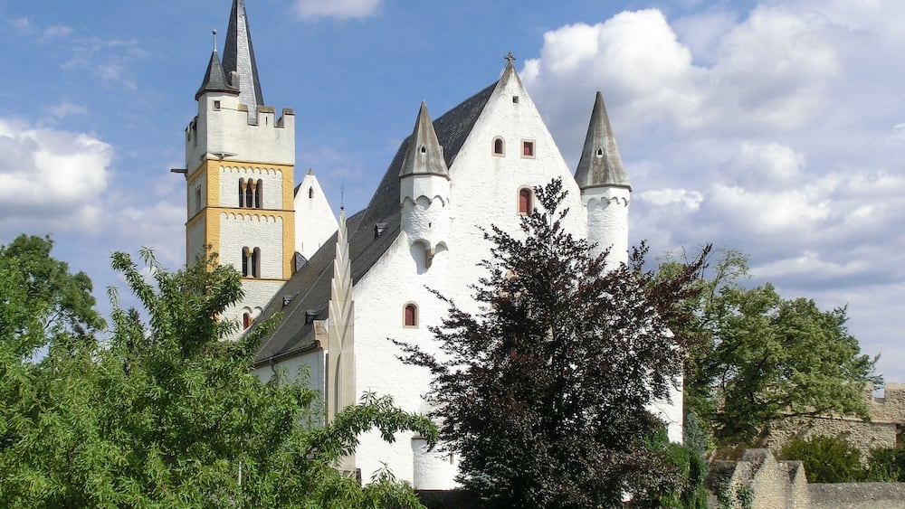 Un château blanc doté de nombreuses tours, dont une tour de l’horloge, et entouré de verdure.