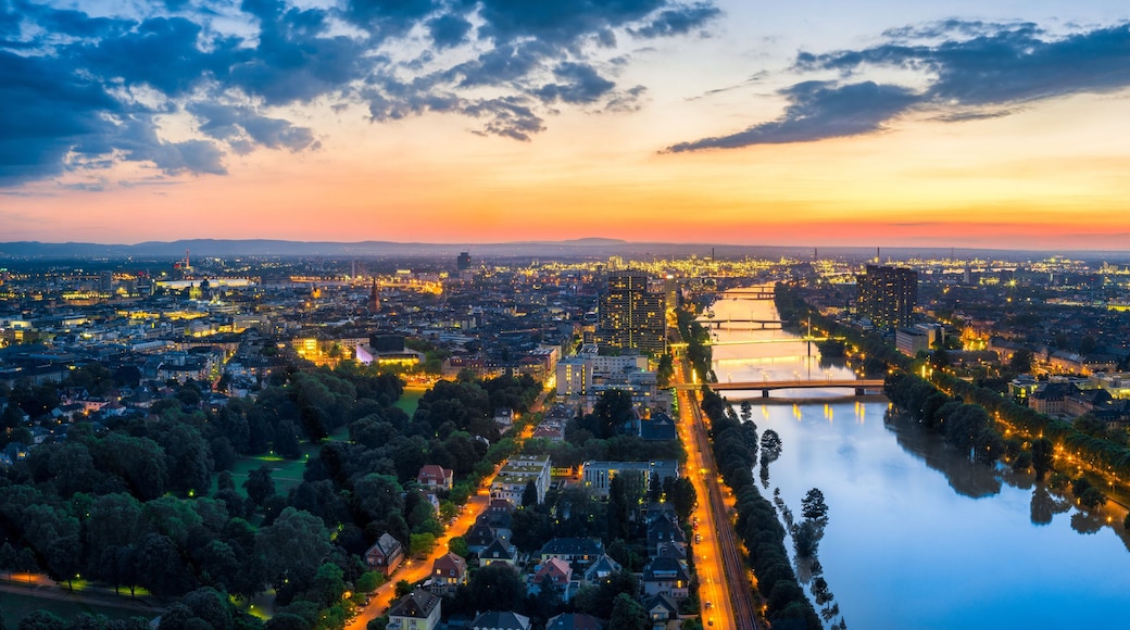 A cityscape at sunset with a river running through it, surrounded by buildings and greenery.