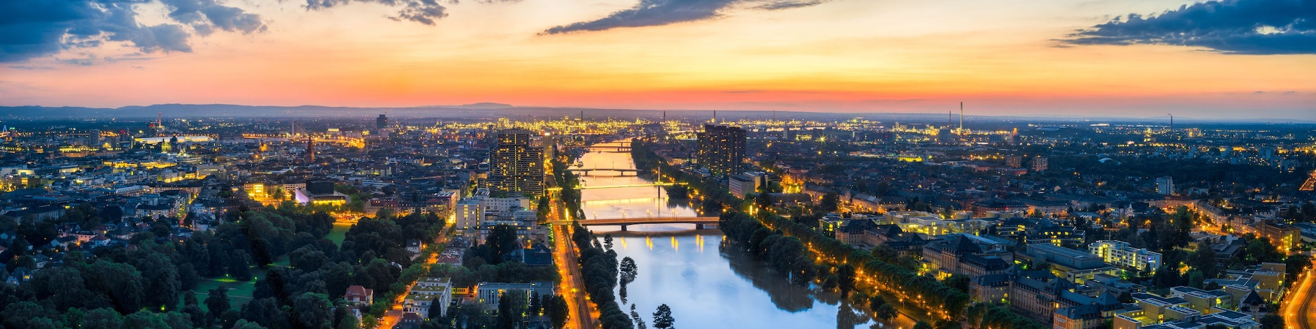 Un paisaje urbano al atardecer con un río que lo atraviesa, rodeado de edificios y vegetación.