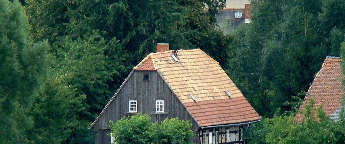 A traditional half-timbered house with a sloped roof, surrounded by lush greenery and trees.