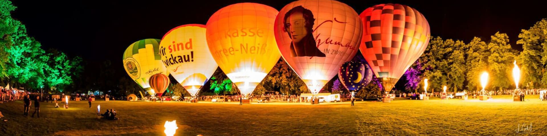 Um festival de balões de ar quente à noite, com balões iluminados e uma multidão de pessoas.