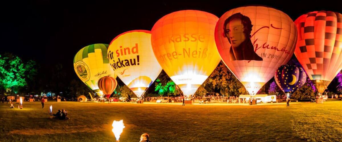 A nighttime hot air balloon festival with illuminated balloons and a crowd of people.