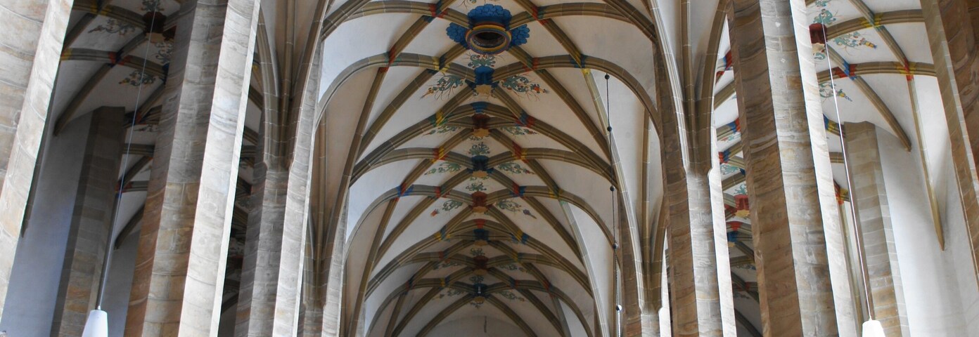 Interior de una catedral con altos techos abovedados, vidrieras de colores y estatuas ornamentadas.
