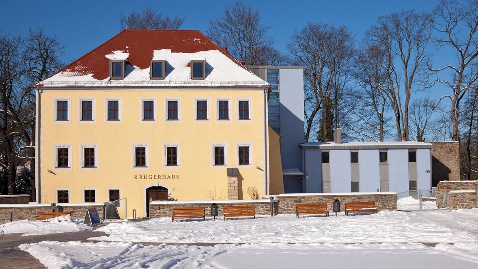 A yellow building with the name "Krügerhaus" and a red roof, surrounded by snow and trees.