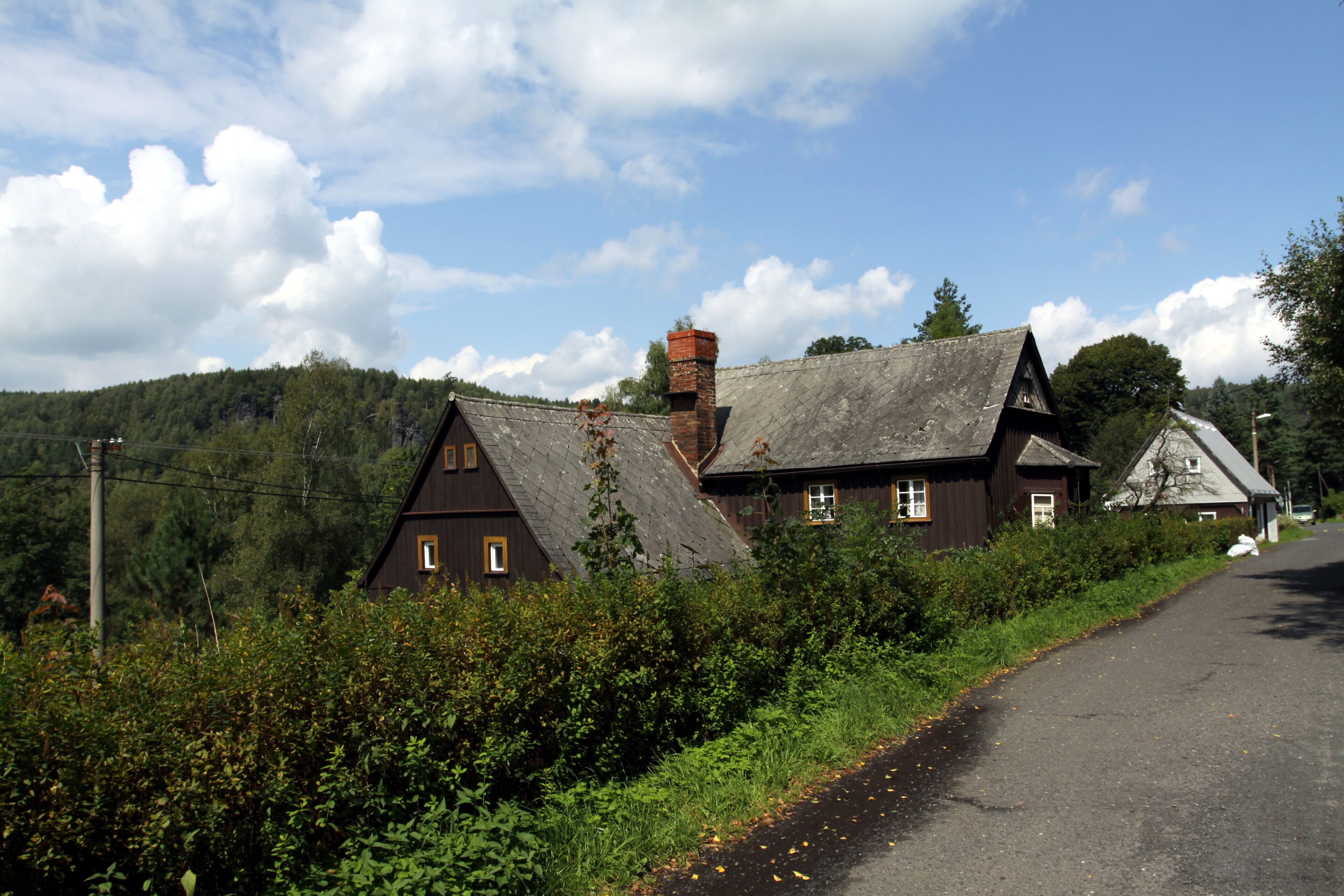 A rural road with a wooden house and a forested hill in the background.