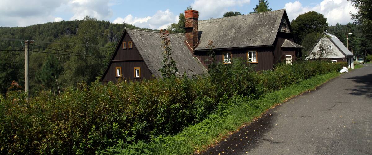 A rural road with a wooden house and a forested hill in the background.