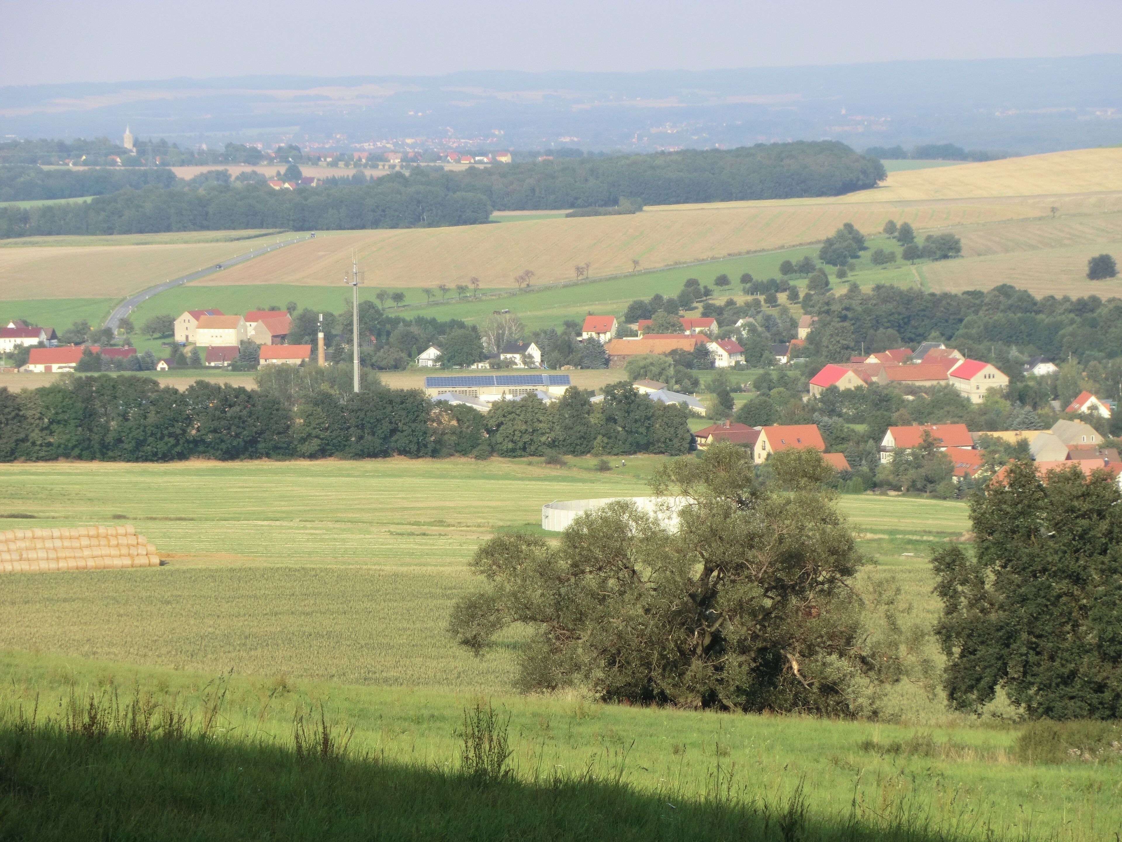 A rural landscape with rolling fields, scattered houses with red roofs, and a distant church spire.