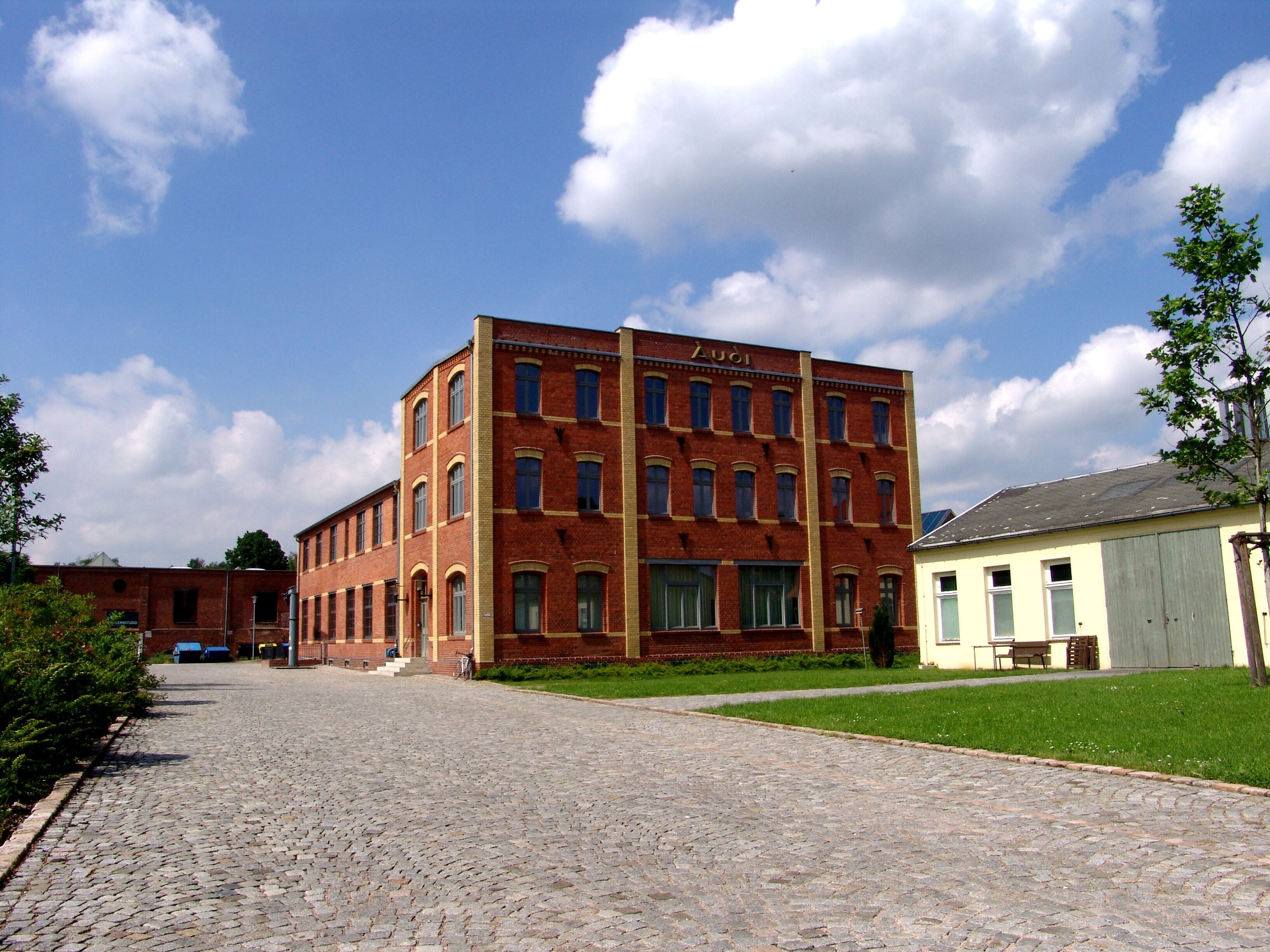 A red brick building with the name "Luoi" on it, a cobblestone street, and a green lawn.